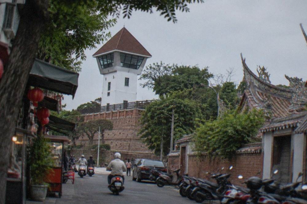 A white-walled fort lookout tower with a pointed tiled roof standing above old brick rampart walls in Anping, Tainan