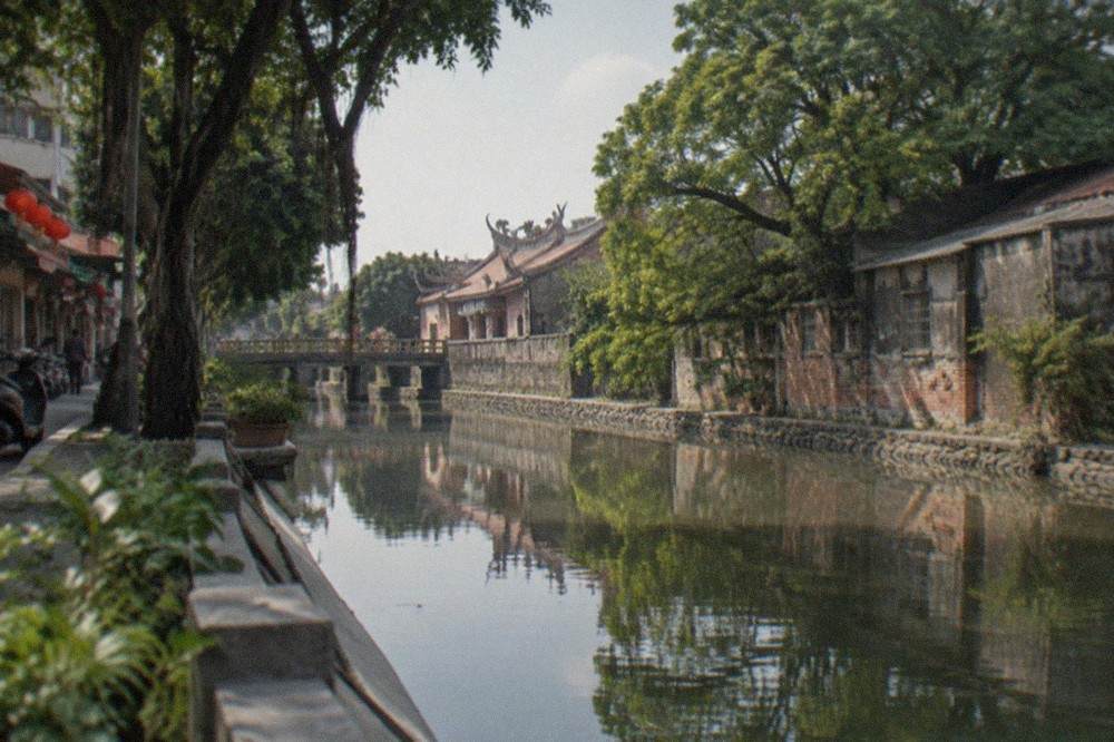 A calm canal in Anping reflecting old warehouse walls and green trees