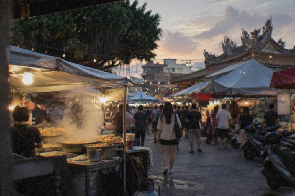 A busy Tainan night market stall at dusk with steam rising from a hot food counter
