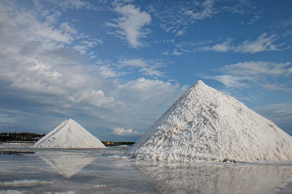 White salt mounds rising above a flat coastal landscape under a wide sky