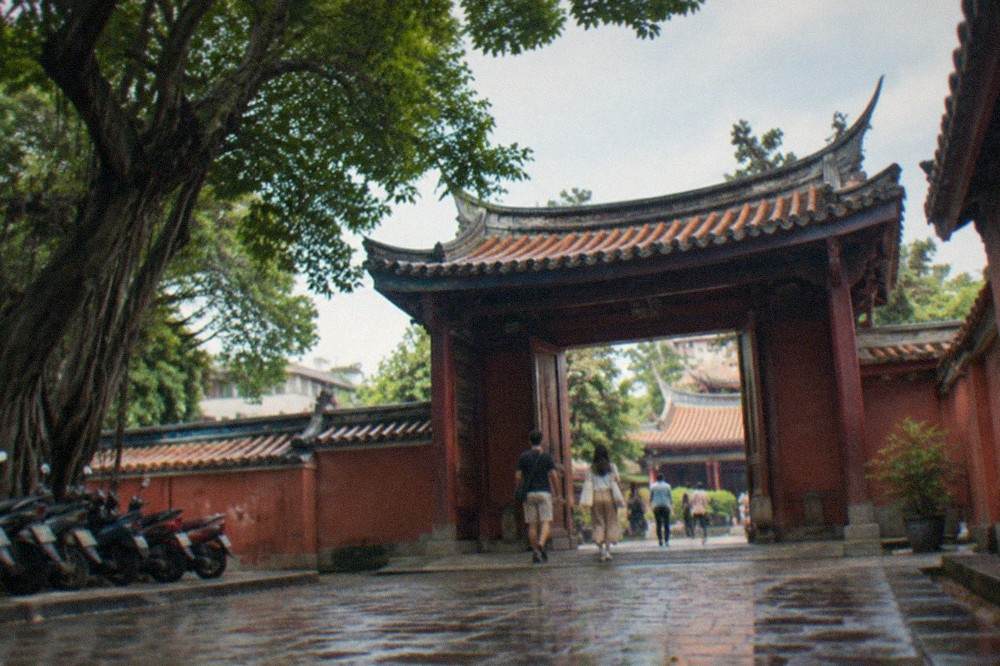 Visitors walking through the gated entrance of the Tainan Confucius Temple on a warm day