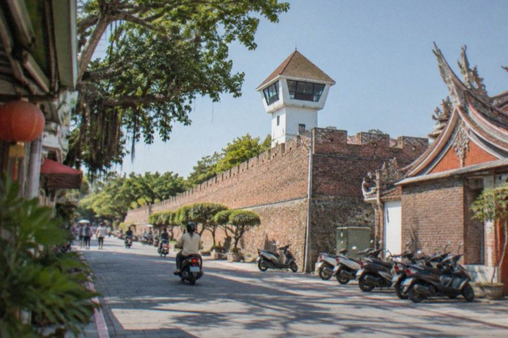 Old brick rampart walls of Anping Old Fort under a clear sky with the white lookout tower behind them