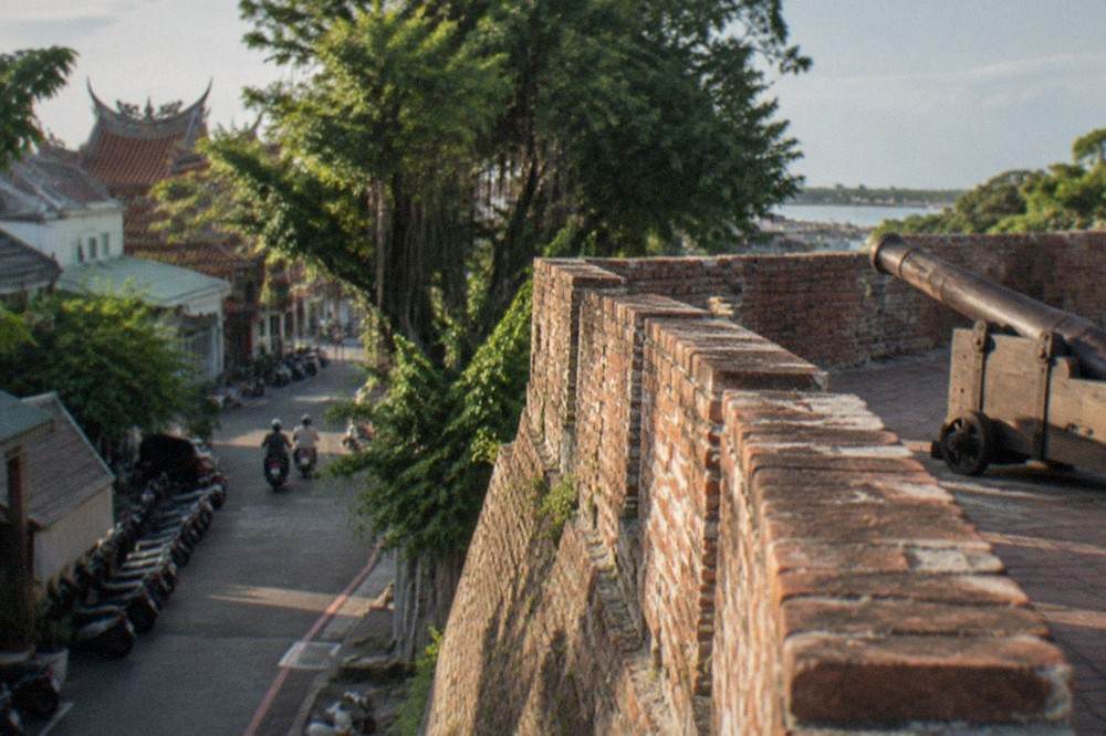 A weathered brick wall section of the old Dutch rampart with explanatory plaque beside a shaded walkway
