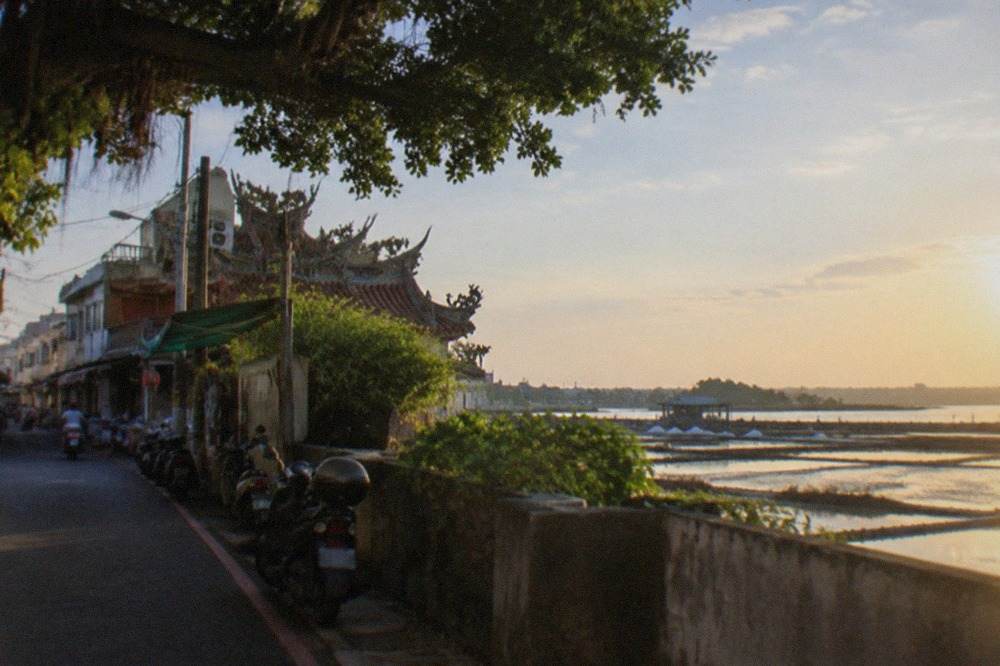 Wide view of flat coastal wetlands with salt pans and a distant temple roof under a bright sky