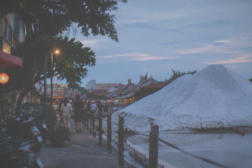 A white mound of salt rising above flat ground with visitors walking a path beside it