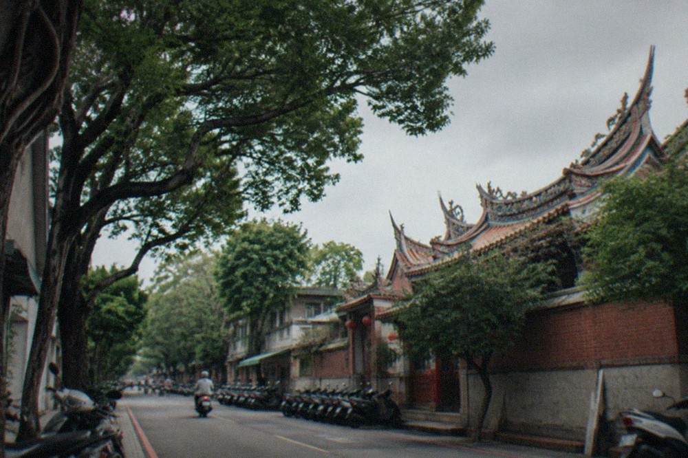A tree-lined university street in Tainan with scooters parked along the curb