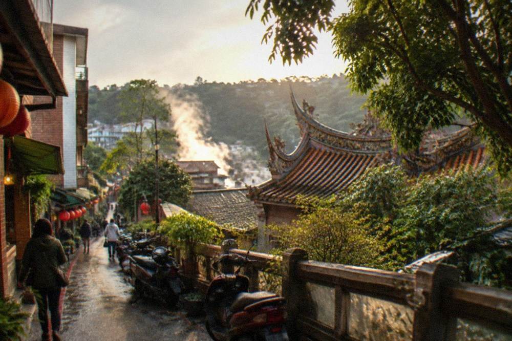 Steam rising from hot spring water among rocks and greenery