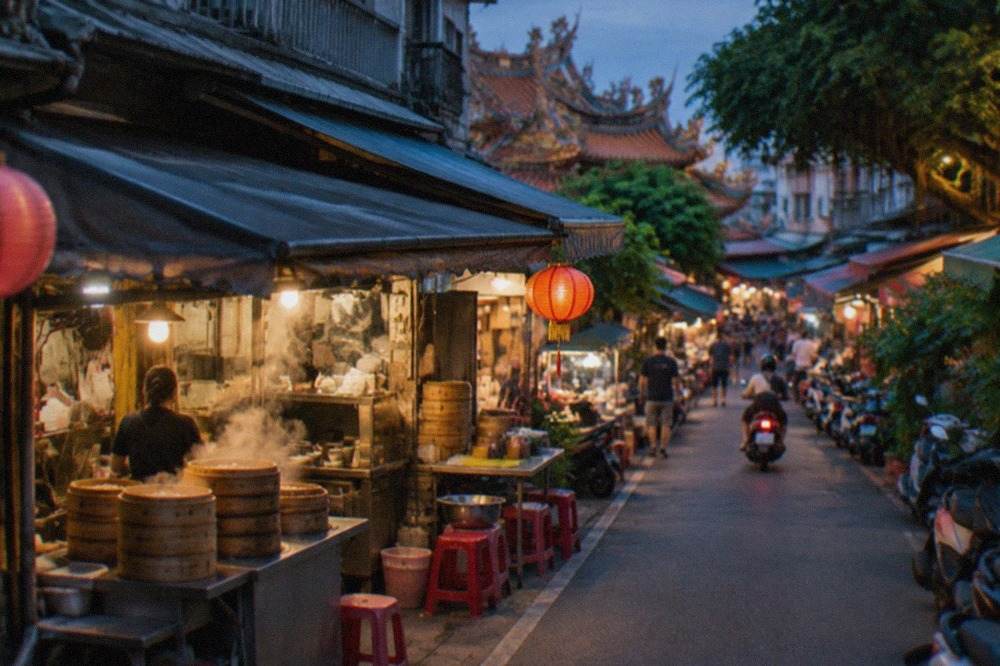 A narrow Tainan street lined with small food stalls and shopfronts under warm afternoon light