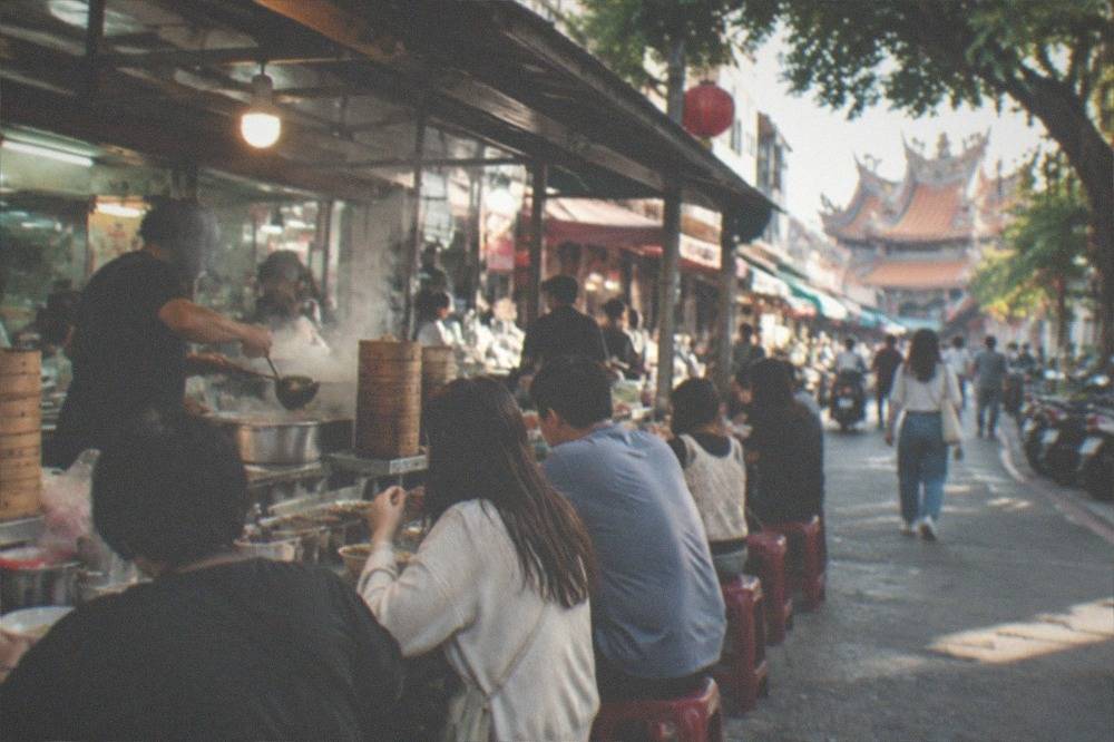 A vendor ladling soup at a counter crowded with customers in the evening