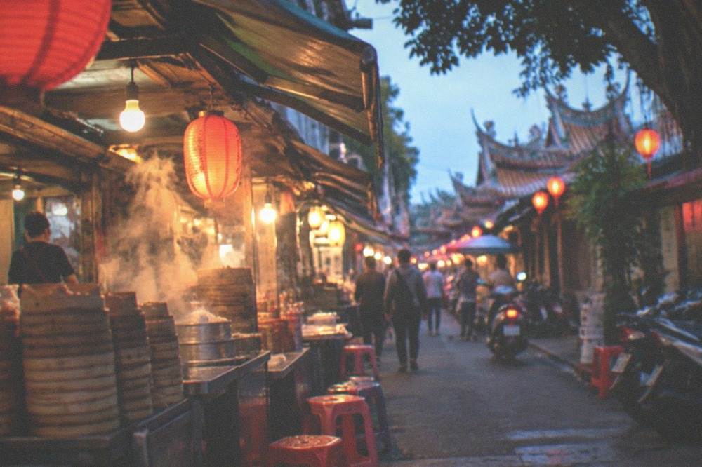 A Tainan alley at dusk with lanterns and small shop signs above the doorways