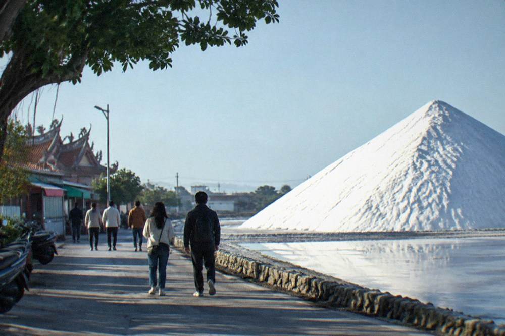 Visitors walking on a path beside a tall white pile of salt under a blue sky