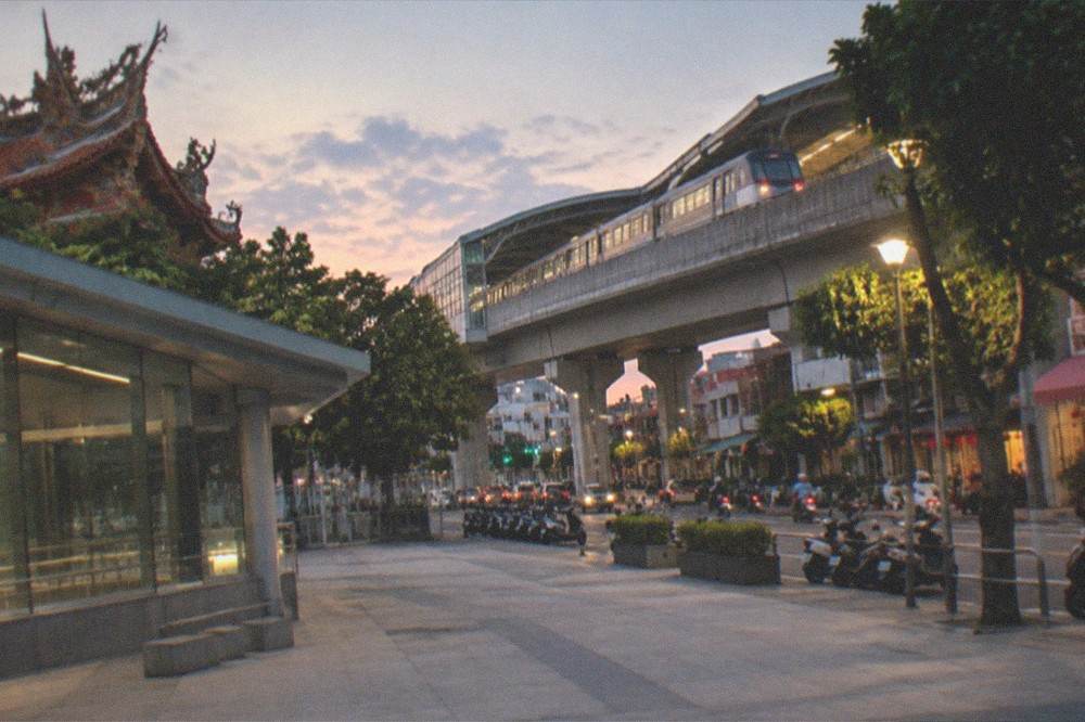 A train departing an elevated station at dusk with city lights beginning to appear