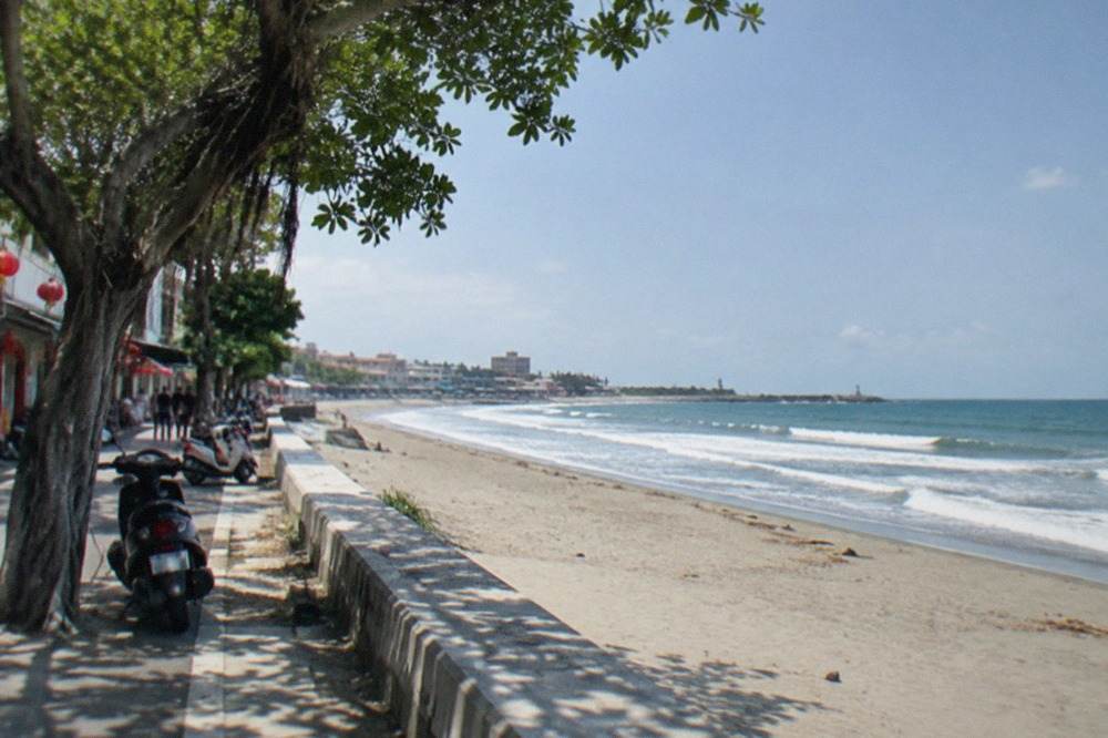 Wide sandy shoreline with waves rolling in and a low coastal skyline under a bright sky