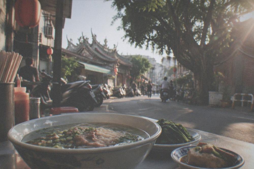 A bowl of noodle soup and small side dishes on a table at a street food stall