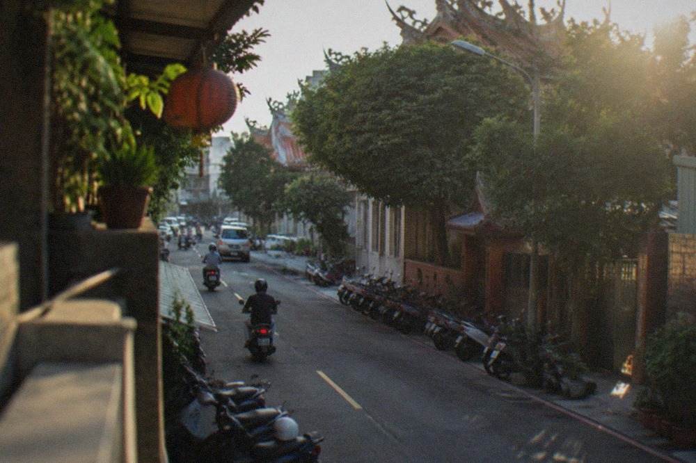 A busy street in a Taiwanese city district with scooters parked along the sidewalk and shop signs overhead