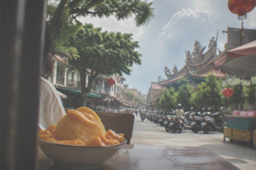 A bowl of mango shaved ice with fresh cut mango pieces on a table