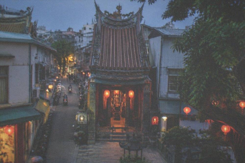 A stone temple courtyard at dusk with lanterns glowing in Tainan