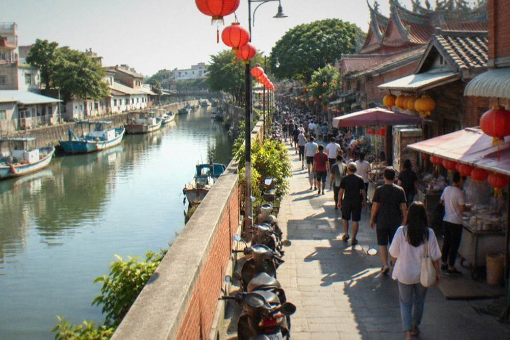 A narrow old street with low brick buildings, red lanterns and food stalls, crowded in the afternoon