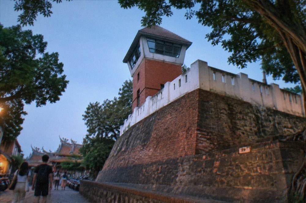 Visitors walking on a stone path beside old fort walls under a clear sky