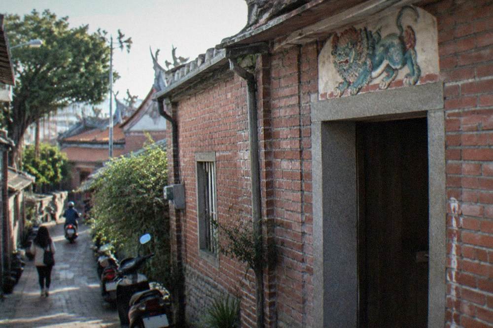 A narrow Anping alley with old brick houses and a small painted sword lion above a doorway