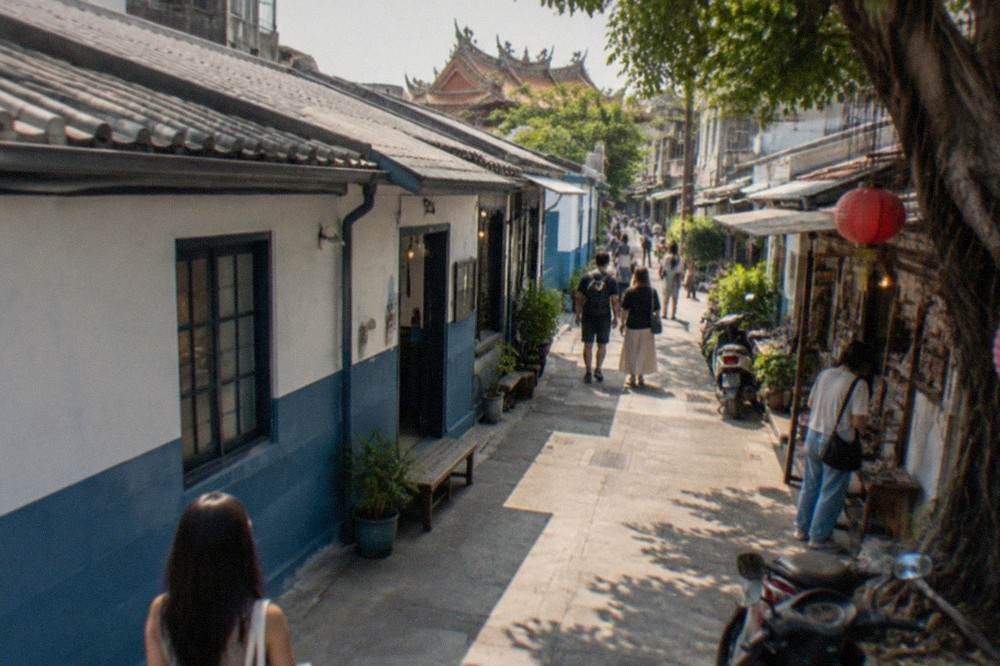 A painted wall and open walkway in a creative park, with small shops and visitors browsing in the evening