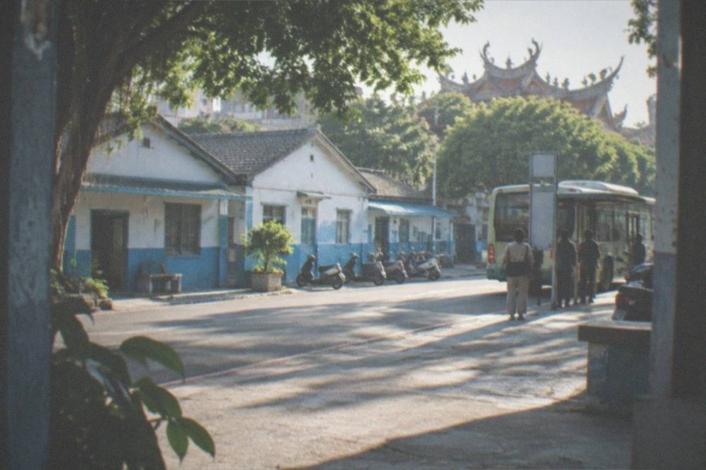 A Tainan city bus at a stop on a tree-lined street with passengers waiting