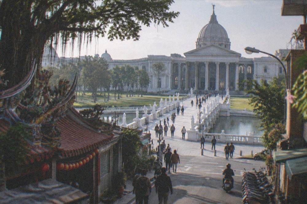 Visitors walking on the plaza in front of the museum entrance between the statue-lined bridge and the doors
