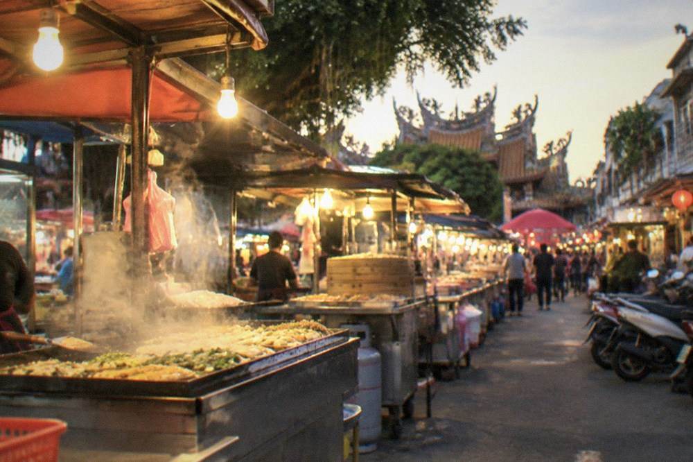 Aerial view of a night market's rows of illuminated stalls and surrounding city streets at dusk
