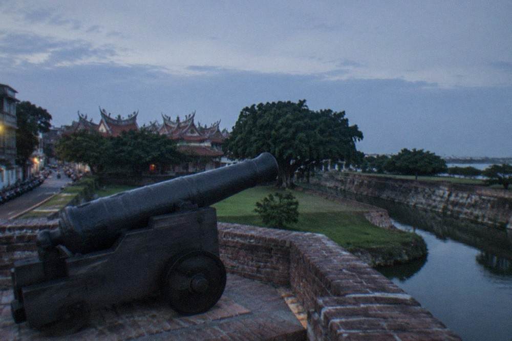 A replica breech-loading cannon mounted on a brick emplacement above a grassy fort interior