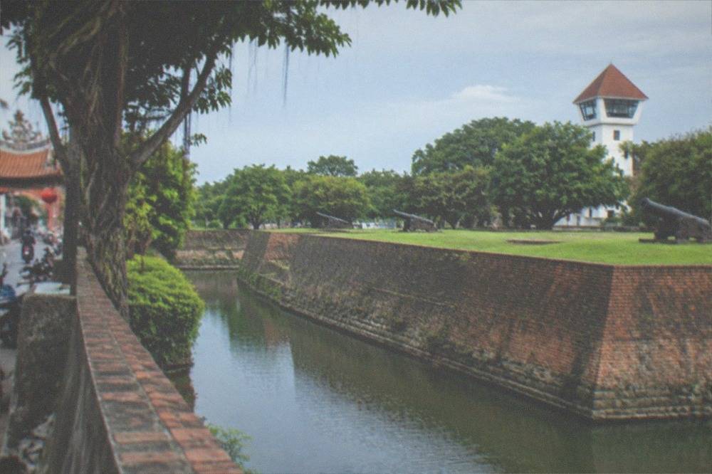 A grassed parade ground inside fort walls with brick rampart walks and shady trees