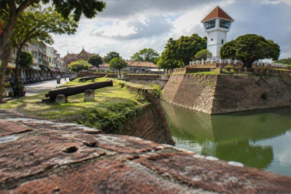 A tall white lookout tower on old fort walls beside a cluster of tiled rooftops