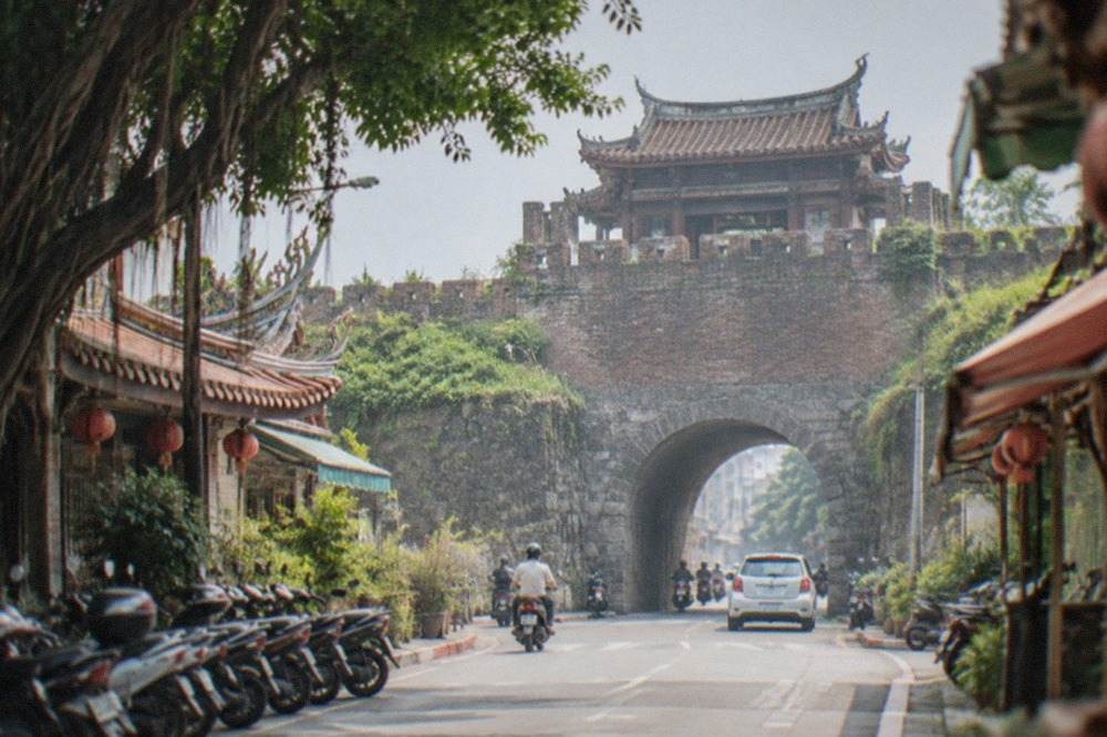 An old stone city gate with arched doorway and crenellated walls under a blue sky