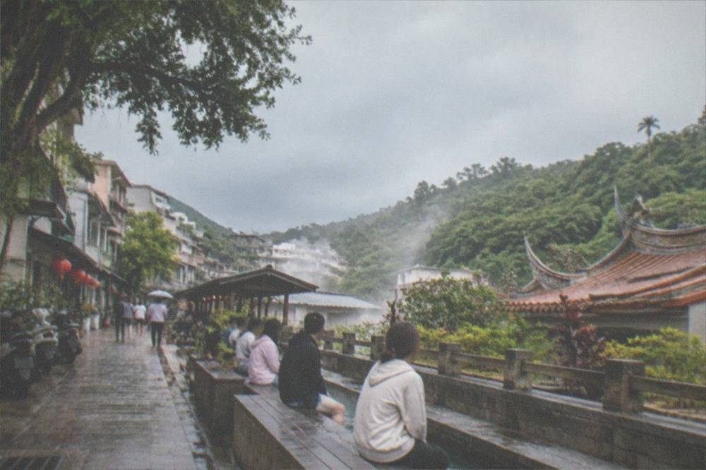 Visitors soaking their feet in a long public foot bath beside a hillside street