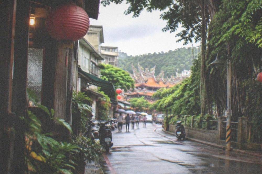 A quiet hillside road winding through green forest toward spa buildings