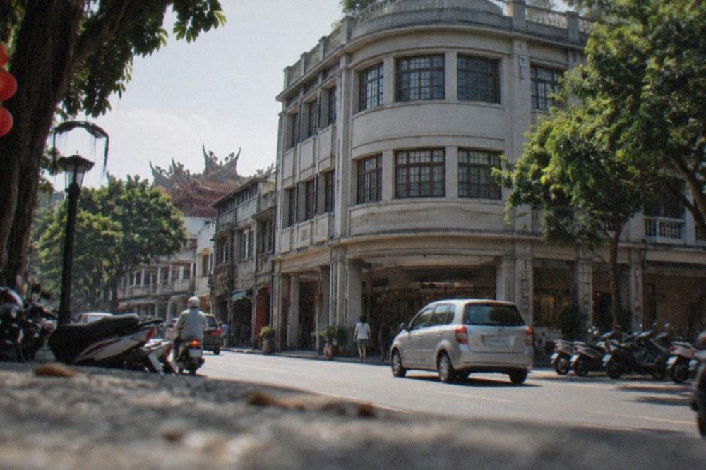 A restored Japanese-era department store building with a curved facade beside a tree-lined street in central Tainan