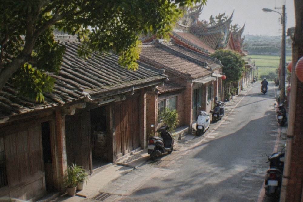 A quiet old street with low brick storefronts and wooden shutters in a rural Taiwanese village