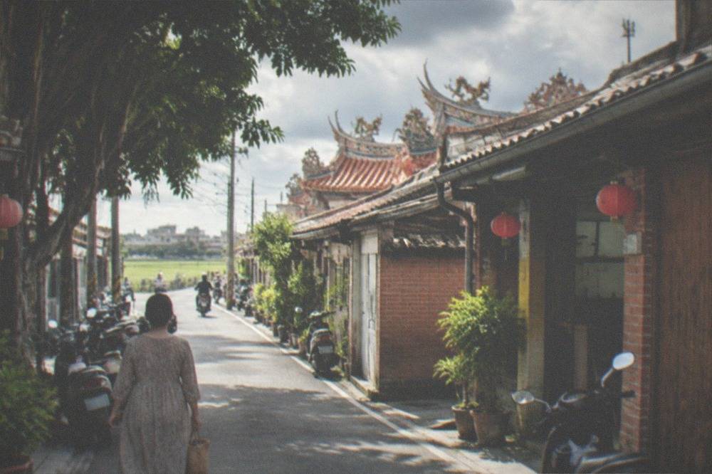 A woman in a traditional qipao dress standing on an old street with brick walls