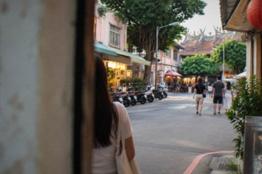 A city street at dusk with lit shopfronts and people walking in the evening