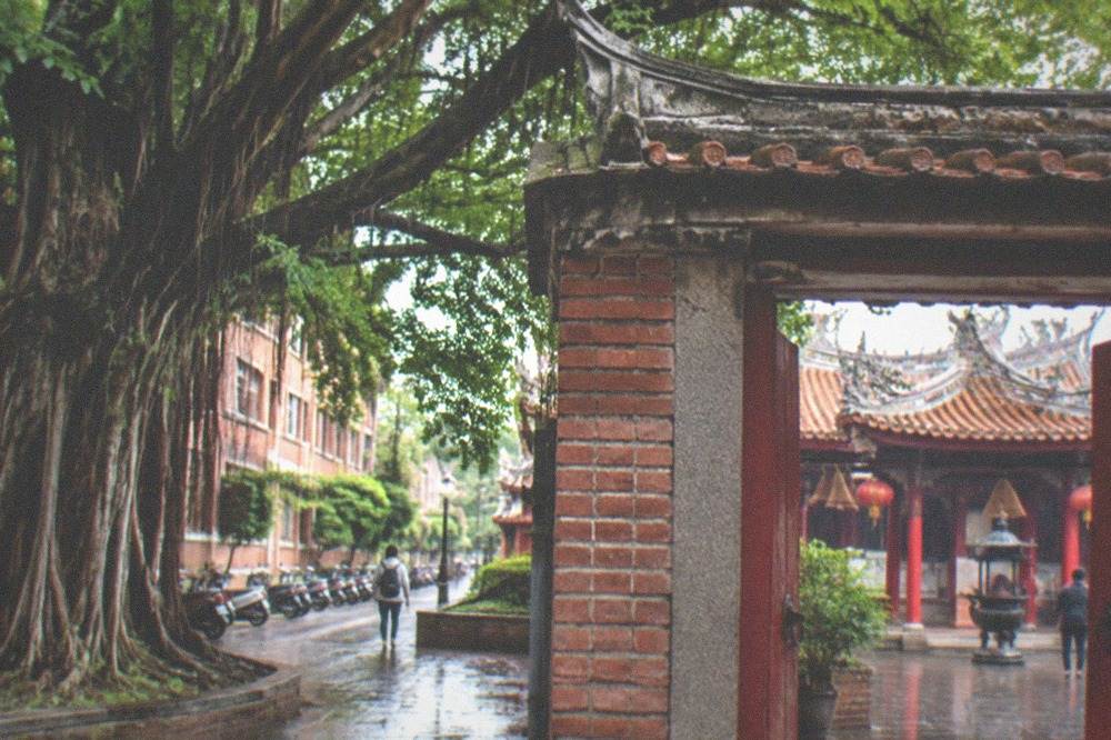 A temple courtyard with red pillars and incense coils seen through a gate
