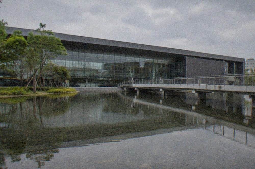 A modern museum building with a large glass facade reflected in a wide shallow pool of water
