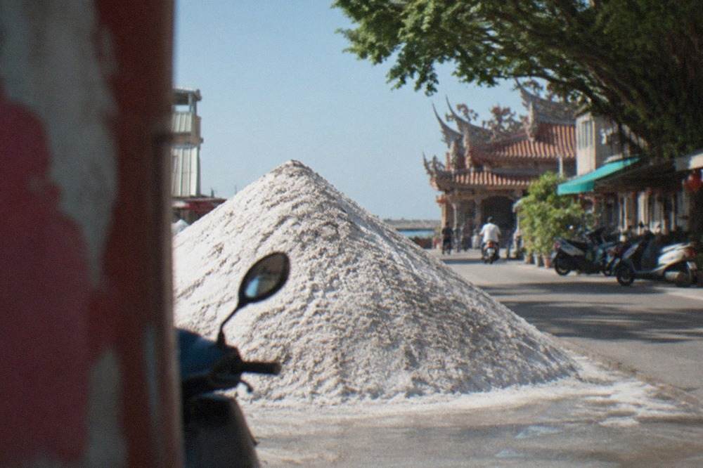 A large white mound of salt rising above a flat coastal plain under a blue sky