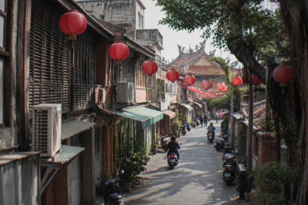 A narrow lane with hanging lanterns and shop signs above restored storefronts