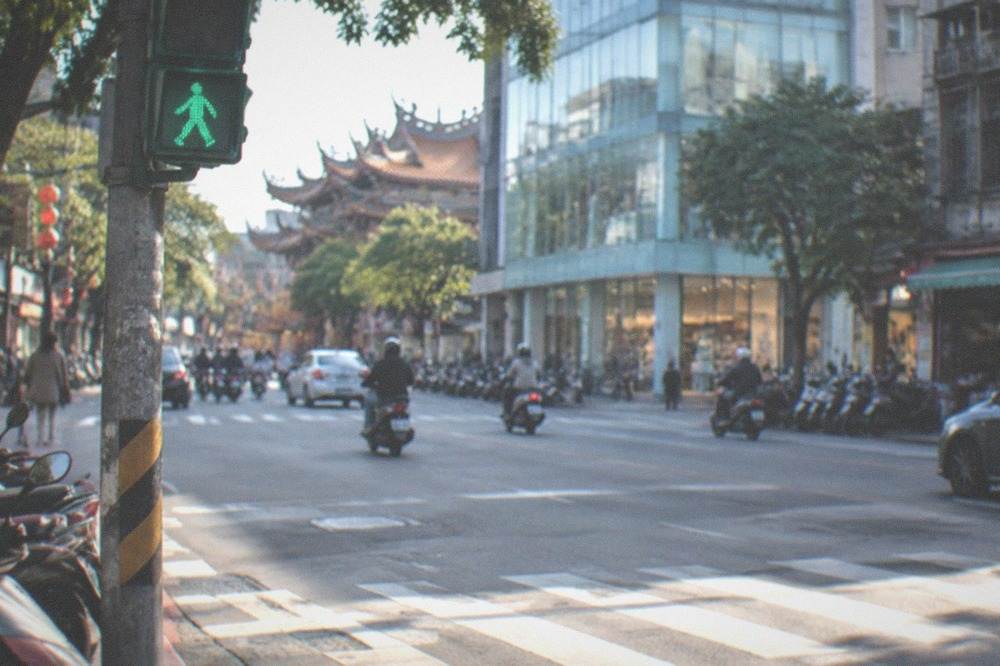 A pedestrian crossing on a wide road with shops on both sides
