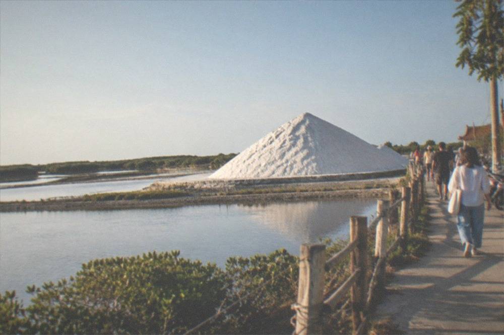 A tall white mound of salt rising above a flat coastal plain with visitors walking a path beside it