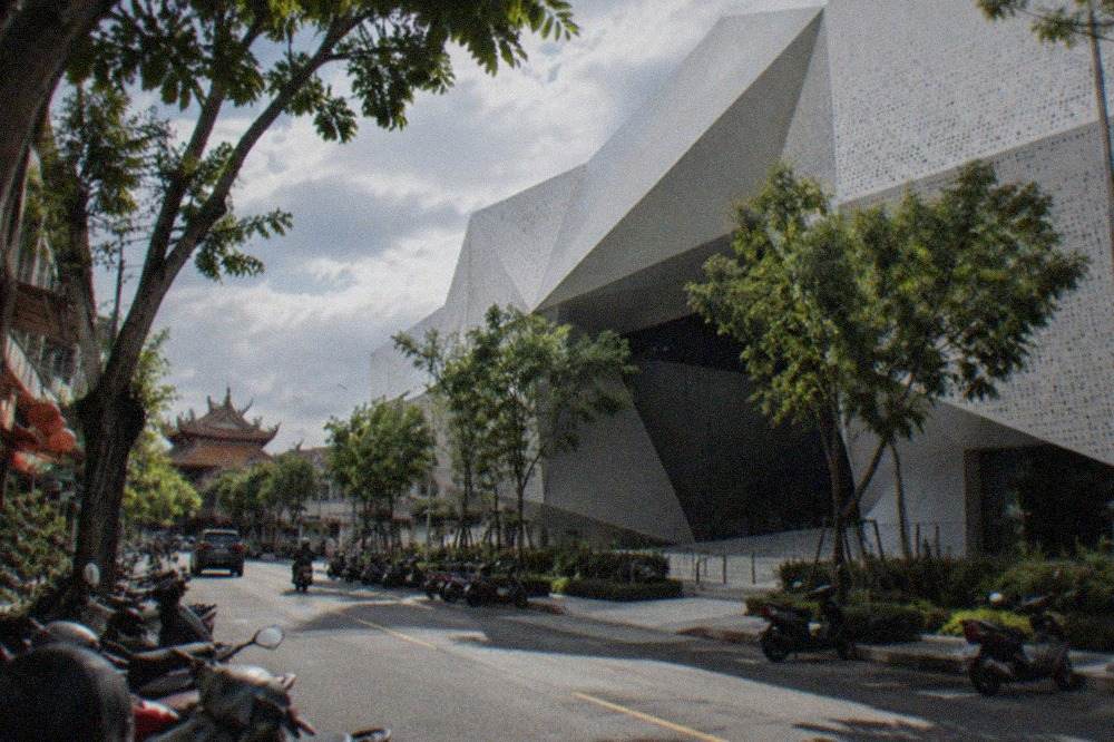 A modern museum building with a white perforated facade beside a tree-lined street in Tainan