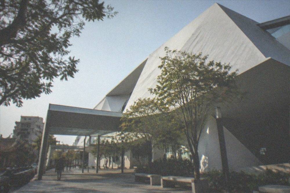 A covered walkway connecting two museum buildings with trees and seating alongside