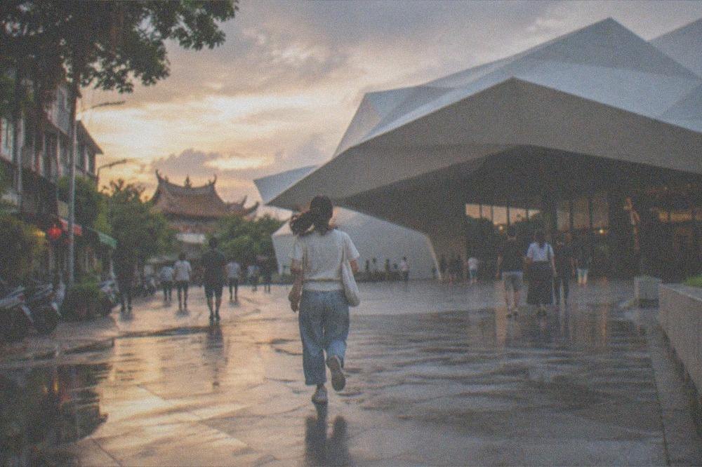 A wide plaza outside a museum entrance with people walking under a warm evening sky
