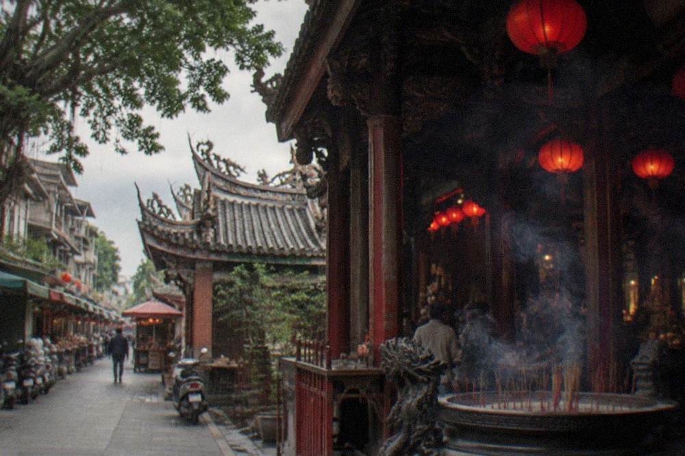 Roofline of an old Taiwanese temple with upturned eaves, dragon ridge decorations and grey tiled slopes