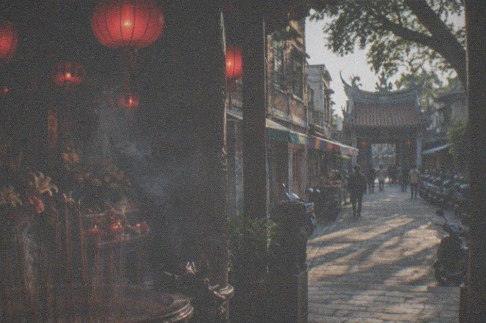 Old Tainan street in late afternoon with long shadows across brick walls and a temple gate in the distance