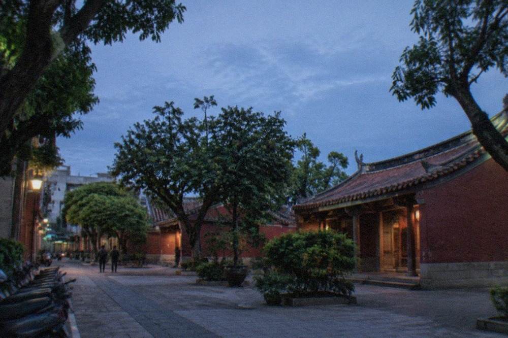 A historic Taiwanese temple courtyard with red walls and a tiled roof beneath trees